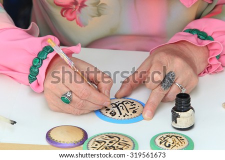 close-up of female hands artist in Tatar national costume, making Arabic calligraphy painting 