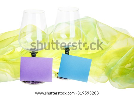 This photo shows close-up of two wine glasses with blue and violet wish cards surrounded by green velvet on the white background.