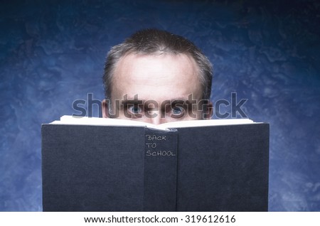 Mature man being focused and hooked by book, reading open book, surprised young man, amazing eyes looking blank cover, back to school written on the spine of the book