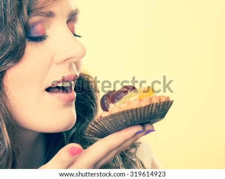 Bakery sweet food indulging and people concept. Cute attractive woman closed eyes holds cake cupcake in hand smelling yellow background