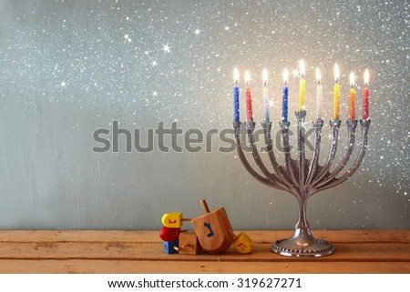low key image of jewish holiday Hanukkah with menorah (traditional Candelabra) and wooden dreidels (spinning top). retro filtered image with glitter
