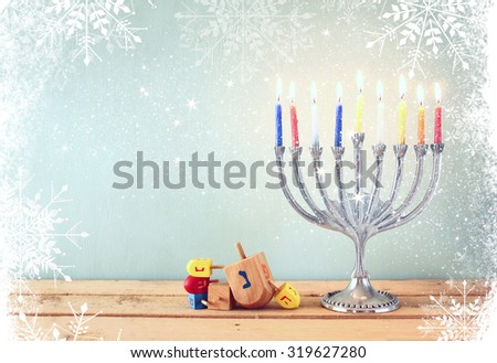 image of jewish holiday Hanukkah with menorah (traditional Candelabra) and wooden dreidels (spinning top). retro filtered image with glitter and snowflakes overlay
