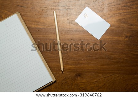 Blank notebook and pencil with white credit card on wooden table. Top view.