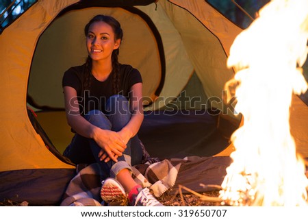 Portrait of a happy woman sitting near bonfire in the forest
