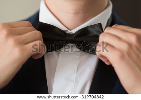 Man's hands touches bow-tie on a suit Royalty-Free Stock Photo #319704842