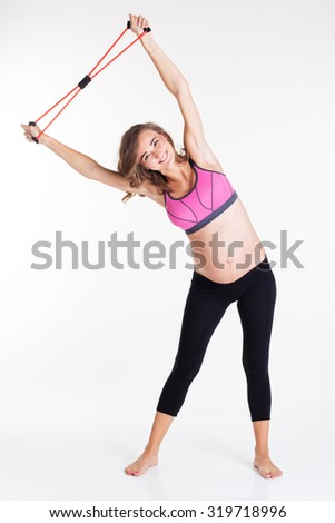Happy pregnant woman doing yoga exercises with special sports rubber band isolated on white in studio 