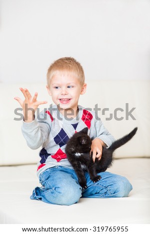 little blond boy playing with a black kitten on a white leather couch
