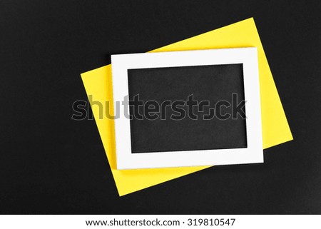 horizontal white photo frame with black field and yellow paper under angle on black background isolated with real shadows