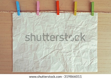 Old wrinkled paper hanging on a rope held by colorful clothespins in front of wooden background.