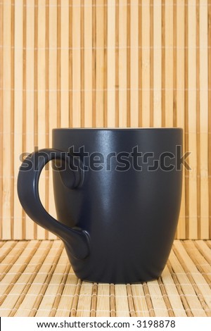 A dark navy blue mug standing upright against a bamboo background. Handle is facing forward to the left. Image is shot at a low angle