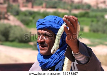 bedouin in morocco with snake in front of ancient village of ait benhaddou