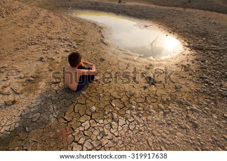Water crisis, Child sit on cracked earth near drying water. Royalty-Free Stock Photo #319917638