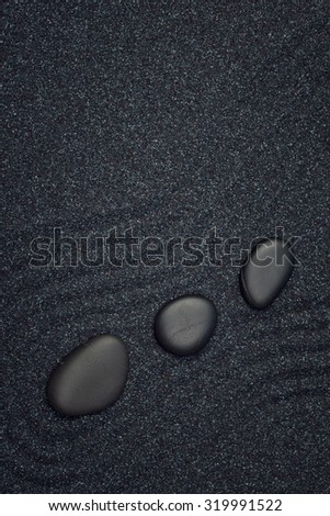 Three black stones aligned in a straight line with waves in a the zen garden