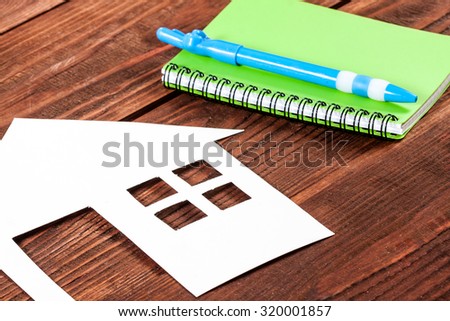 White paper house figure with notebook on wooden background.
