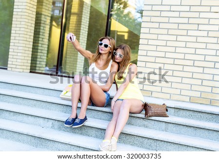 Two sisters on the steps of the institute are doing self, social networking, glasses and denim shorts. Happy smiling resting, fashion lifestyle of girls, teenagers.