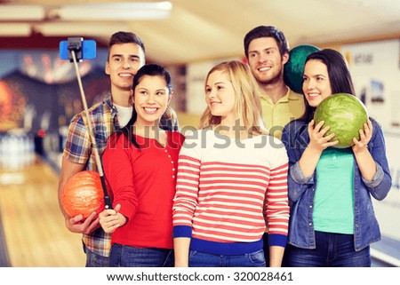 people, leisure, sport, friendship and entertainment concept - happy friends taking selfie with smartphone on monopod in bowling club