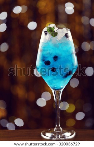 Glass of cocktail with ice on blurred lights background