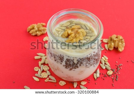 Vegan overnight oats in a jar on red background. Mixture of rolled oats, chia seeds, walnuts, sunflower seeds, soy yogurt, almond milk and agave syrup.