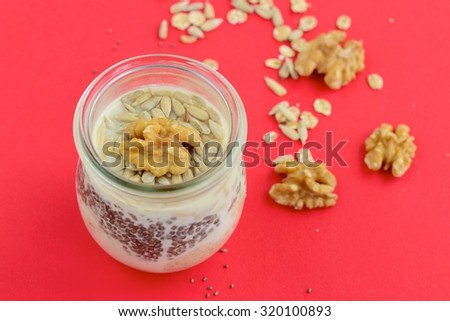 Vegan overnight oats in a jar on red background. Mixture of rolled oats, chia seeds, walnuts, sunflower seeds, soy yogurt, almond milk and agave syrup.