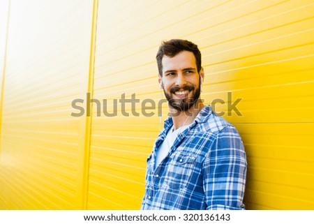 young happy man casual dressed with headphones and smart phone on yellow background