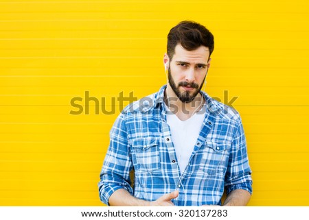 young man casual dressed with headphones and smart phone on yellow background