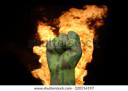 fist with the camouflage texture near the fire on a black background