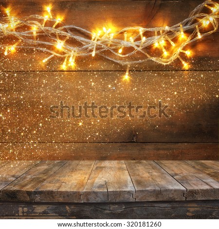 wood board table in front of Christmas warm gold garland lights on wooden rustic background. filtered image. selective focus. glitter overlay