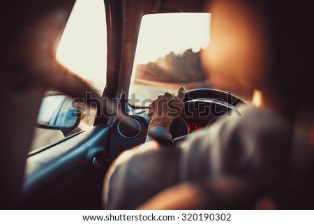 Man driving car, hand on steering wheel, looking at the road ahead,sunset. Royalty-Free Stock Photo #320190302
