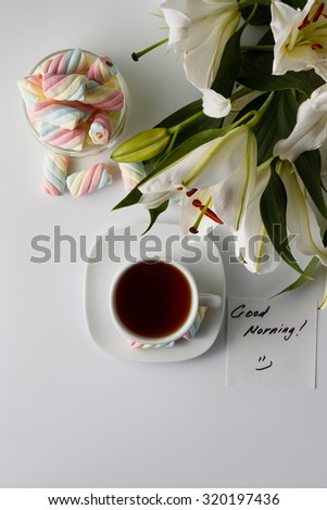 Breakfast concept. Cup of tea, white lily and note good morning