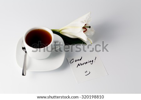 Breakfast concept. Cup of tea, white lily and note good morning