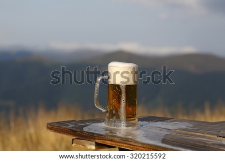 One glass mug with lager or porter tasty frothy beer on wooden table top sunny day outdoor on natural with mountain hills and yellow dry grass background, horizontal picture