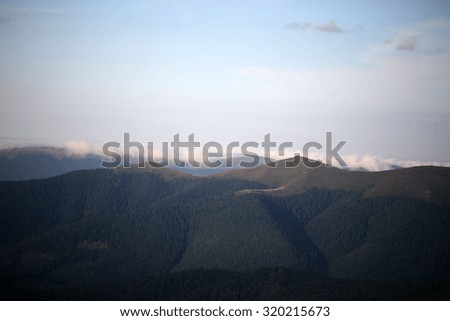 Beautiful spaciousness landscape view from high hill top on many mountain humps with deep green forests and cloudy grey blue sky on sunny natural background, horizontal picture