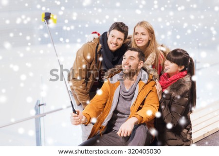 people, friendship, technology and leisure concept - happy friends taking picture with smartphone selfie stick on skating rink