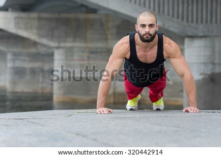 Professional fitness athlete trainer. Muscular male sportsman is training himself. Man is doing pushups. Outdoors fitness sport concept. Street workout