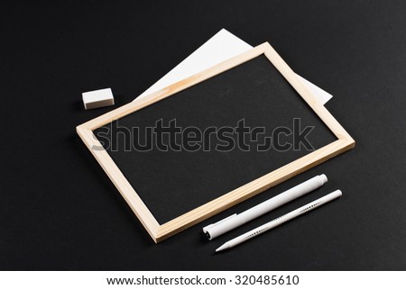 wooden frame with black field with marker and white pencil and eraser on black paper. Mockup. Real photo for you text