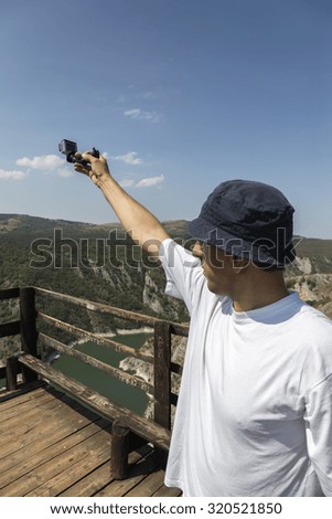 Photographer shooting landscape with small action camera. Made with shallow depth of field.