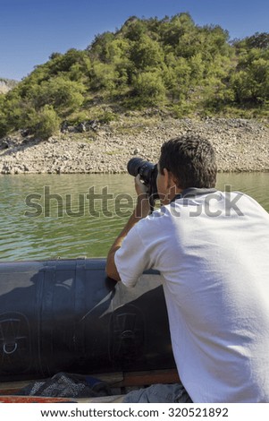 Photographer in boat on the river, shooting outdoors. Professional photographer in action with telephoto lens. Made with shallow depth of field.