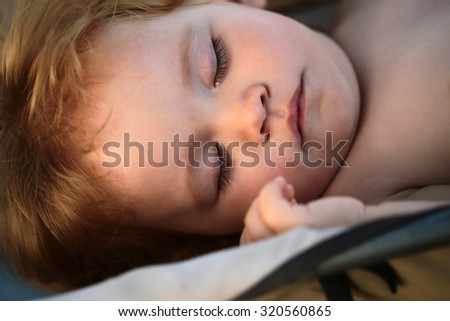 Closeup portrait of one cute relaxing lovely small male child with blonde curly hair and round cheeks sleeping in natural day light, horizontal picture