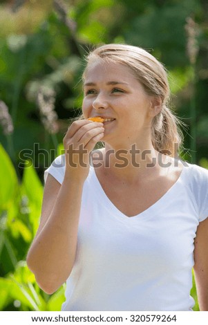 relaxation outside - happy young woman eating fruit for healthy diet with green exotic environment background, summer daylight