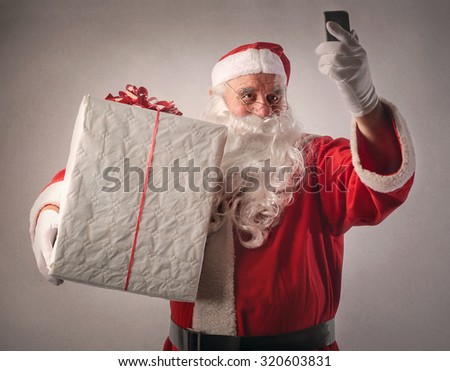 Santa Claus holding a big present and a smartphone