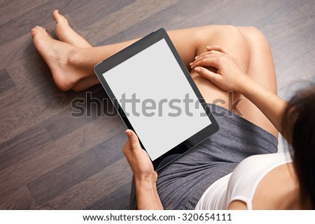 Woman using tablet computer while sitting on a wooden floor. View from above. Clipping path included.