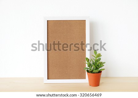 Blank white wooden frame and small tree on wood board over white cement wall background, template ,mock up