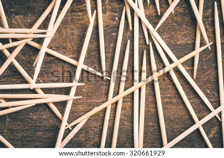 Many toothpicks lying in pile facing different directions on a dark wooden surface.