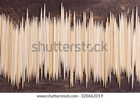 Big pile of toothpicks lying in an uneven horisontal line on dark wooden surface.