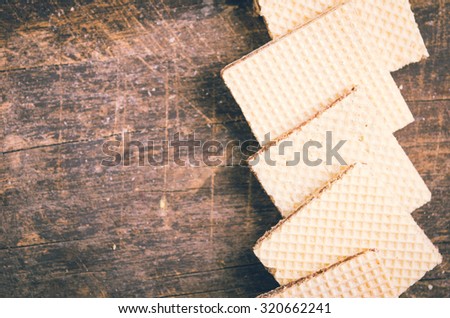 Closeup square cookies lying overlapping each other in a row across wooden surface.