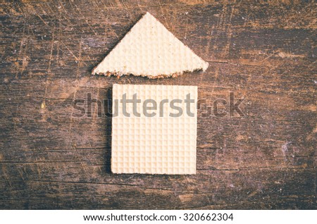 Simple house design illustrated by using rectangular and a triangular cookie on wooden surface.