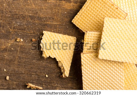 Pile of square cookies with one lying on the side half eaten, wooden surface.