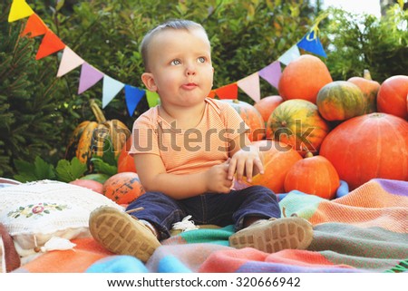 Cute little boy among the pumpkins. Halloween. Garland, Pumpkin and boy. A boy in a shirt and jeans. Kindergarten. Celebration. Parenting. Thoughtful kid. Children's portrait. Feast of All Saints