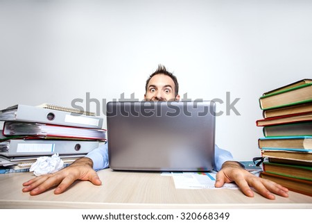 Funny photo of businessman wearing shirt. Businessman working with laptop and looking out from behind. He sitting at table full of documents. Isolated on white background