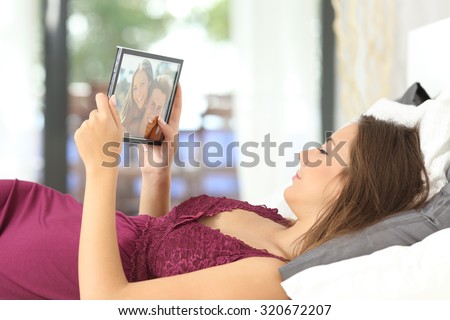 Longing woman looking a picture of her boyfriend in a frame on the bed at home